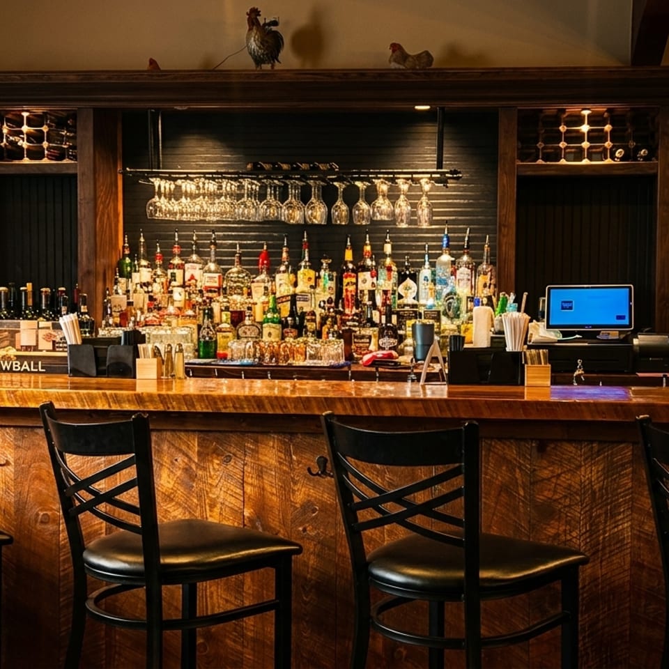 A rustic wooden bar with many liquor bottles, hanging glasses, and four black bar stools.