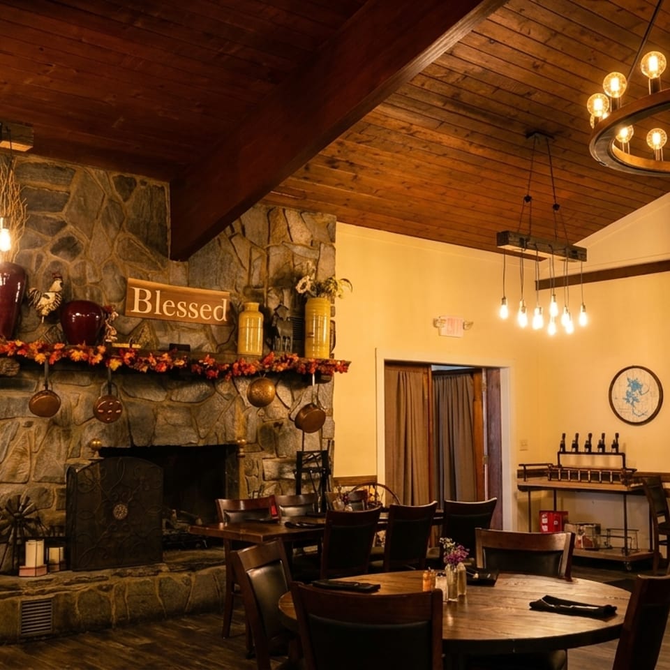 Cozy restaurant interior with a stone fireplace, wooden tables, and warm lighting from chandeliers.